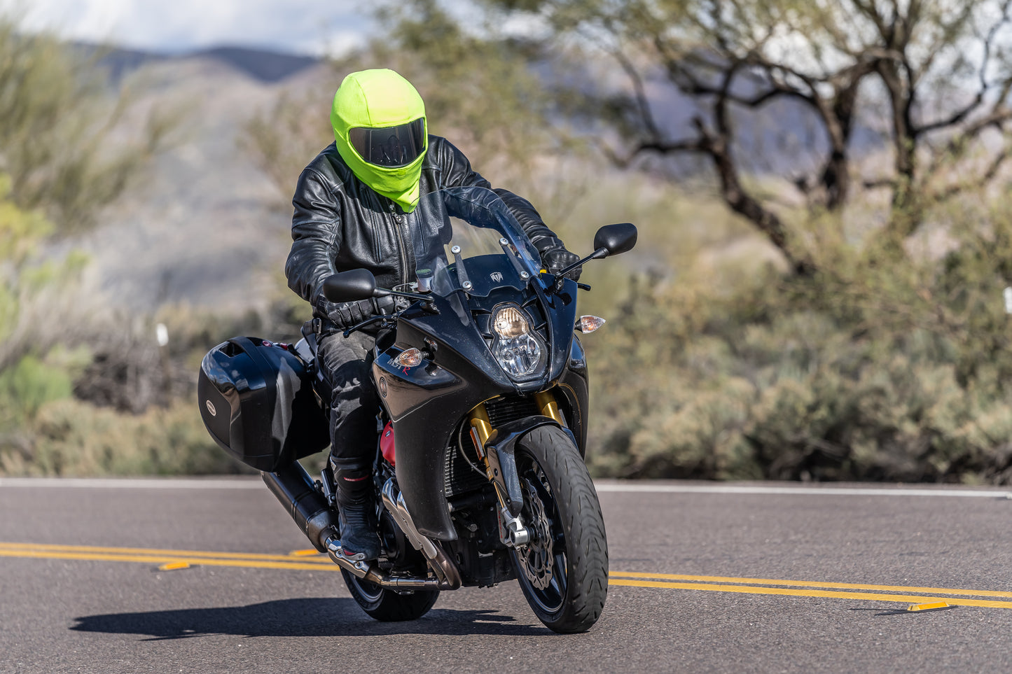 Man wearing green fleece helmet cover turning tight curvy road on motorcycle 