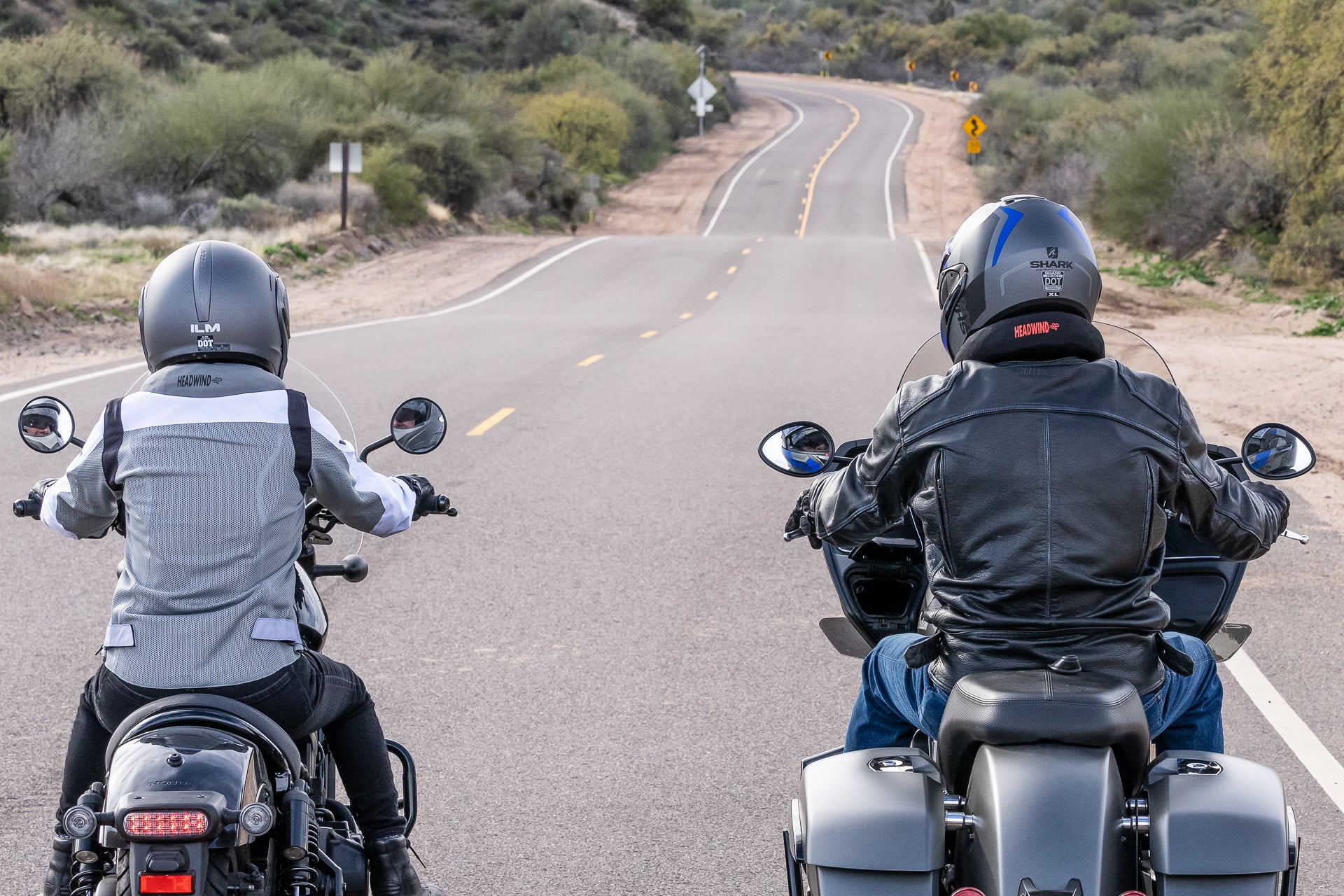 Two people riding down curvy road on motorcycles with neck ring on below helmet