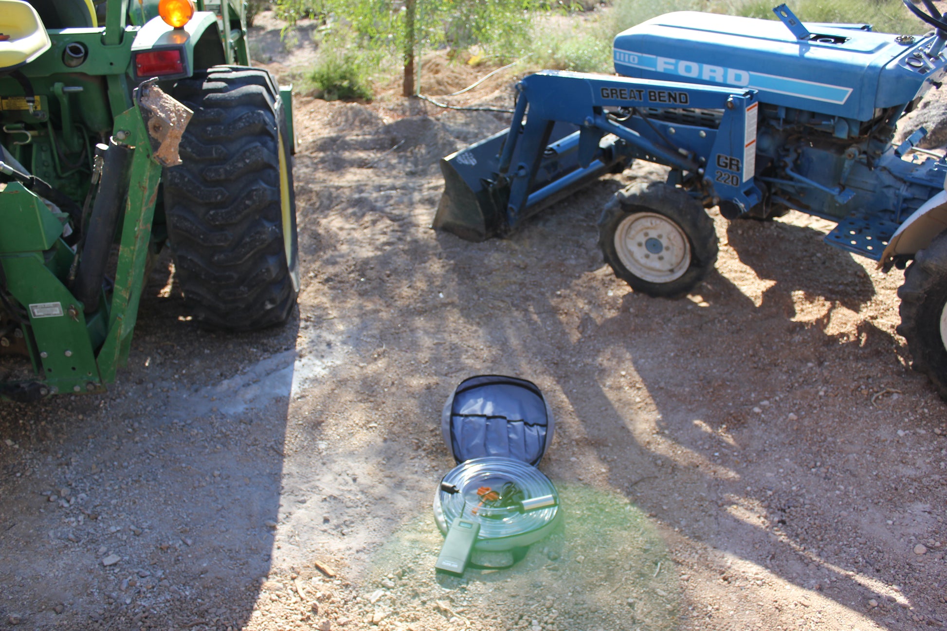 Submersible siphon in carry bag being used between two tractors to move fuel with battery